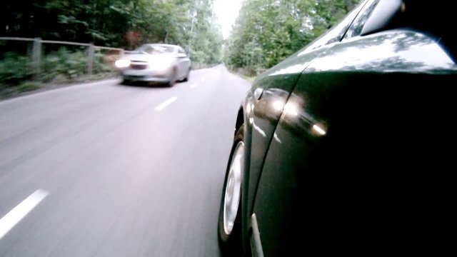 Car goes on asphalt road near trees in wood