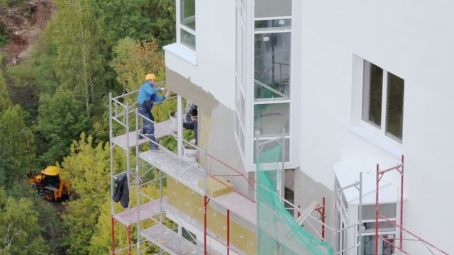 Excavator rides near construction site where worker stands