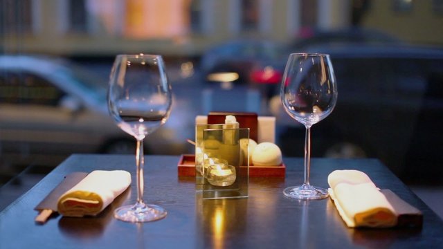 Candle burns at table with glasses and chopsticks, evening street traffic behind window