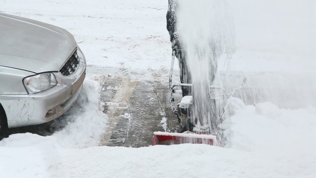 Worker removes snow near car with hand snowblower 