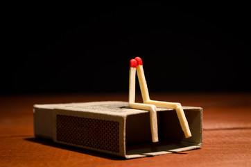 Two match humans sitting on matchbox on a dark background - 80213247