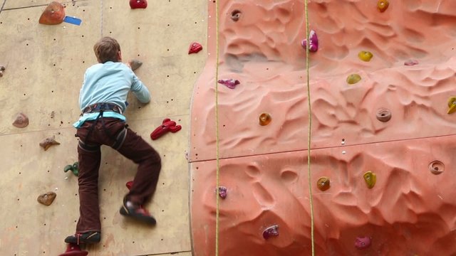 Boy-beginner climbs up on vertical rock-climbing wall