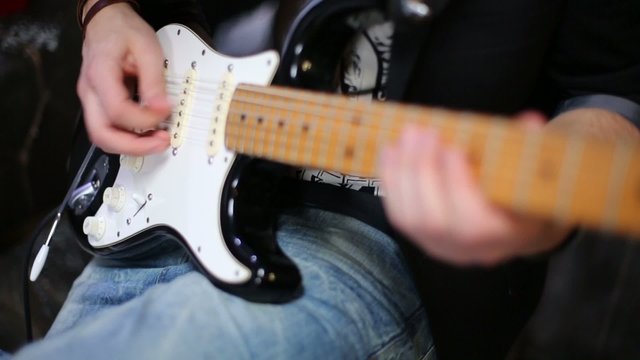 Young man in jeans plays electric guitar at studio