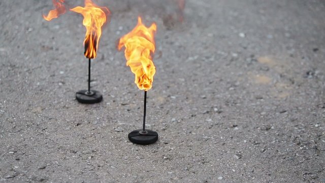 Two burning and smoking torches stand on asphalt road