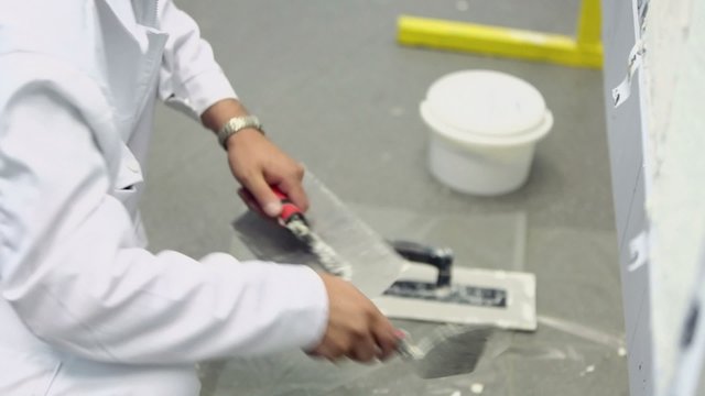 Worker in white uniform cleans spattle from putty, closeup
