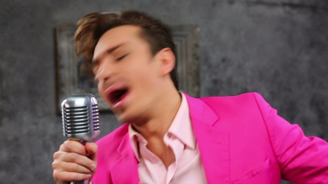 Young man in pink suit with dental braces sings into microphone