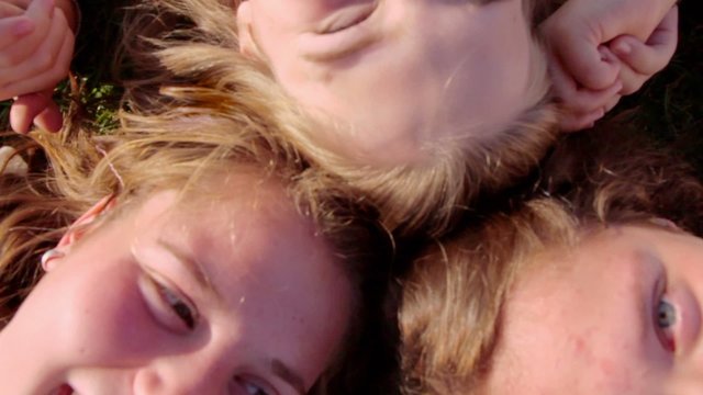 Three girls lay on grass at sunny summer day, zoom from above