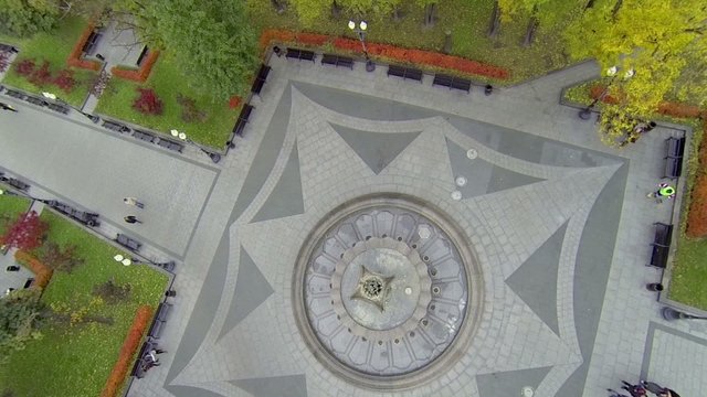 People walk by park near fountain with ornamental pavement