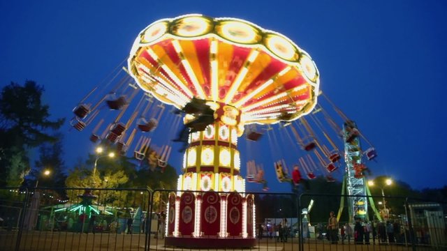 People fly on chairs during ride on round spins carousel and Ferris wheel