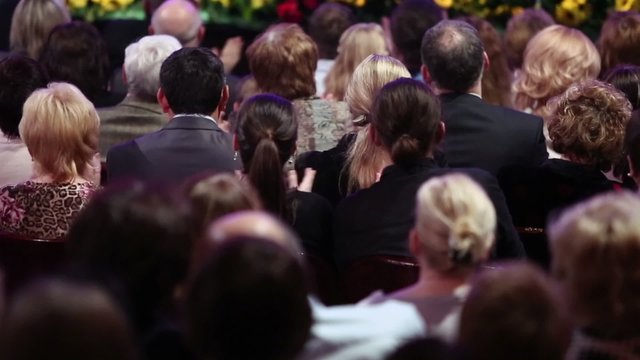 Many men and women sit in theater and applaud