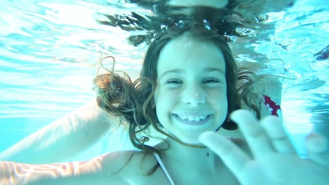 Little girl dances underwater in bar in pool with her mother