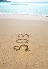 SOS distress sign written in sand of an island beach above water