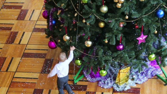 Little boy in mask run around Christmas tree with colorful balls