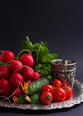 fresh vegetables and greens (cucumber, radish, tomato, lettuce, spinach) on the metal tray on a black background