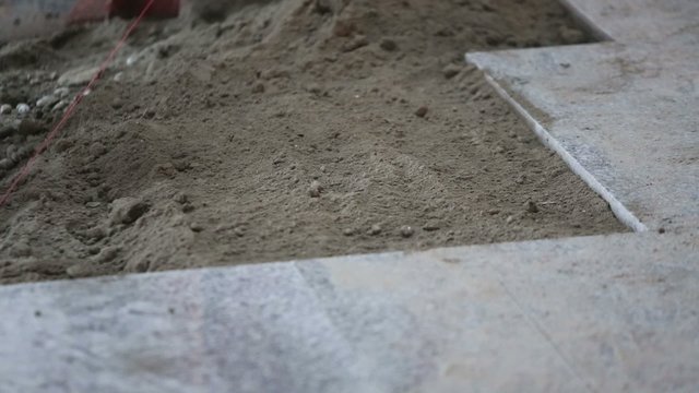 Experienced worker aligns sand for laying marble tiles