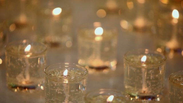 Several candles burn in glasses, closeup view in dark
