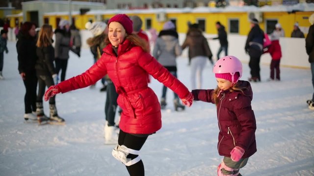 Happy mother and daughter skate at ice rink on sunny winter day