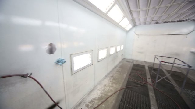 Atomizer in empty paint-spraying booth with metal walls for cars