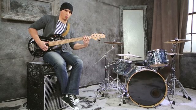 Young musician plays bass electric guitar sitting on amplifier