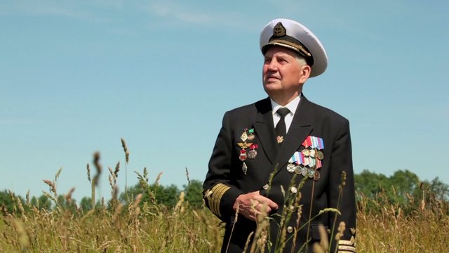 Old man in marine uniform stands in field near forest