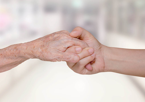 Young nurse holding old patient hand in hospital
