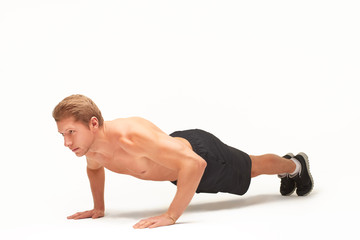 Muscular shirtless sportsman making push-ups on palms in studio