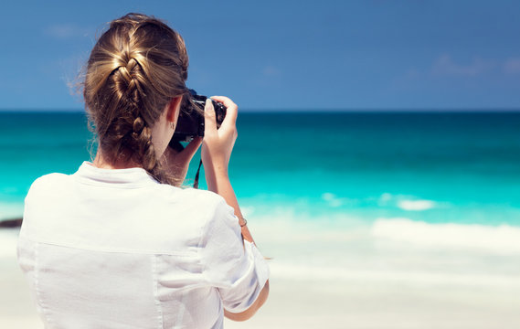 woman on tropical beach taking photo with mirrorless camera
