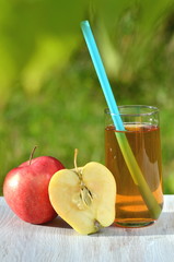 szklanka soku jabłkowego i jabłko na stole w ogrodzie