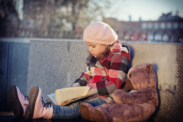 Fototapeta premium little girl reads book in a toy bear sitting on a bench. 
