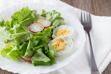 Green salad with radish and hard-boiled egg on white plate