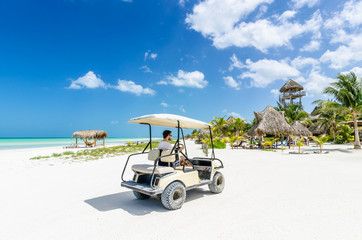 Young man driving golf cart along tropical sandy beach