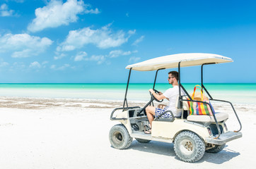 Young man driving golf cart along tropical sandy beach