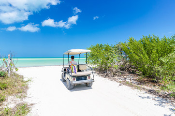 Young man driving on a golf cart at tropical white sandy beach