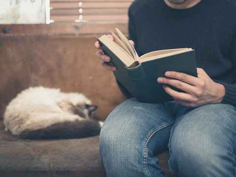 Young man sitting on sofa with cat is reading