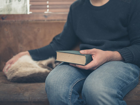 Young man sitting on a a sofa with a cat and a big book