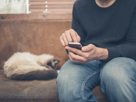 Young man sitting on sofa with cat using his smartphone