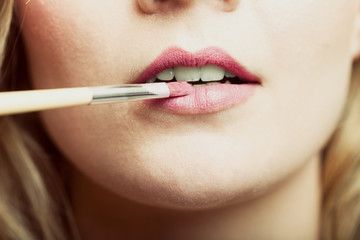 Part of face. Woman applying pink lipstick with brush