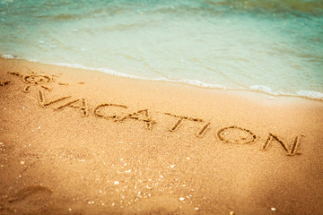 The word vacation written in the sand on a beach