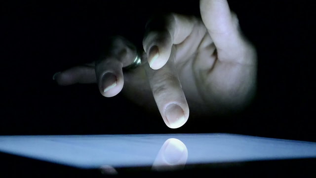 Finger touching tablet computer touch screen at dark