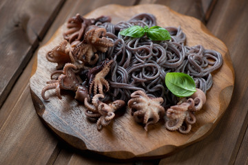 Fototapeta premium Wooden cutting board with octopuses and black rice noodles