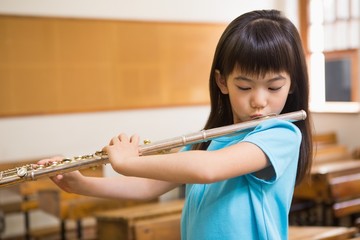 Cute pupil playing flute in classroom - obrazy, fototapety, plakaty