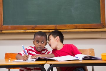 Cute pupils writing at desk in classroom