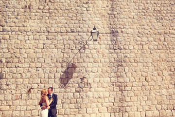 Fototapeta na wymiar groom and bride in front of a big brick wall