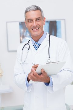 Happy doctor holding clipboard and smiling at camera