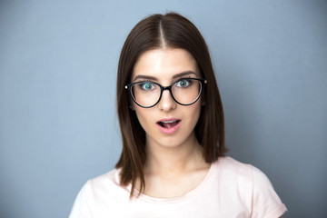 Fototapeta premium Surprised young woman in glasses over gray background