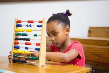 Cute pupil using abacus in classroom