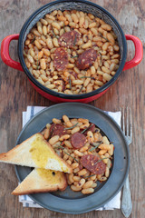 Beans and chorizo cooked with rosemary leaves on a tin plate.