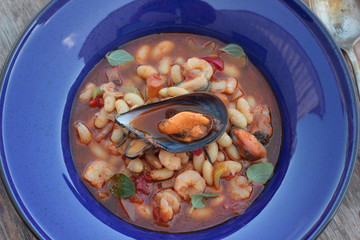 Beans and chorizo cooked with seafood on a blue plate.