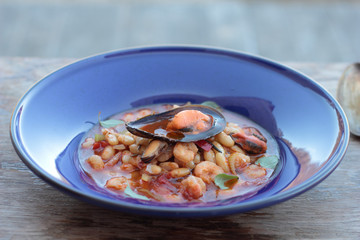 Beans and chorizo cooked with seafood on a blue plate.