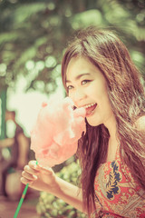 Cute Thai girl is eating pink candyfloss with joy in vintage col